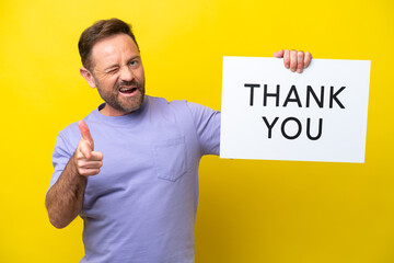 Middle age caucasian man isolated on yellow background holding a placard with text THANK YOU and...