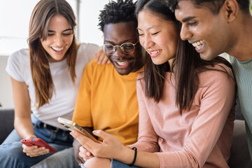 Multiethnic young group of teenage friends using mobile phone together at home. Diverse millennial...