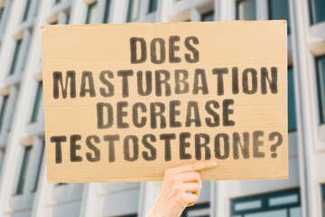 The question " Does masturbation decrease testosterone? " is on a banner in men's hands with blurred background. Risk. Sexual. Stress. Bodybuilding. Metabolism. Deficiency. Diagnosis. Molecular
