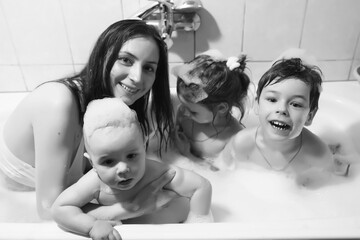 Mom washes the children. Mom and children are taking water procedures in the bathroom. Foam, spray.