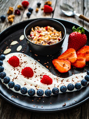 Yogurt with strawberries, blueberries, raspberries and muesli in bowl on wooden table
