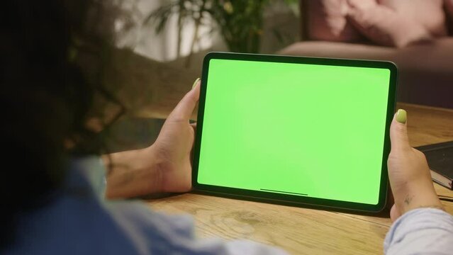 Chroma Key Without Touching or Swiping. Back View of Woman Holding Green Screen Smartphone Watching Content. Girl Using Tablet sitting in the living room in the evening, Browsing Internet, Watching