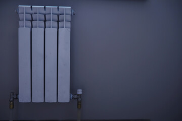 White modern aluminum radiator battery for hot water heating, on the background of a wall in the interior of an apartment or office space.