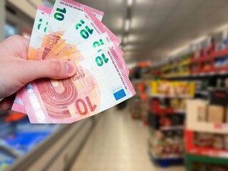 Euro banknotes in hand and grocery store in the background. Increase in food prices in Europe....
