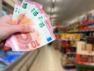 Euro banknotes in hand and grocery store in the background. Increase in food prices in Europe. Rising inflation
