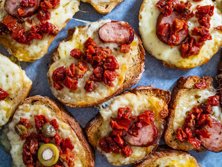 Tasty sandwiches - baked bread with sausage, cheese, sun dried tomatoes and greens on wooden table
