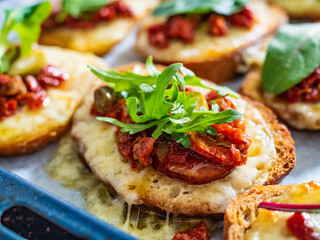 Tasty sandwiches - baked bread with sausage, cheese, sun dried tomatoes and greens on wooden table
