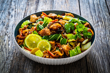 Asian food - chicken nuggets, noodles, stir fried vegetables, soy sauce and mushrooms on wooden table
