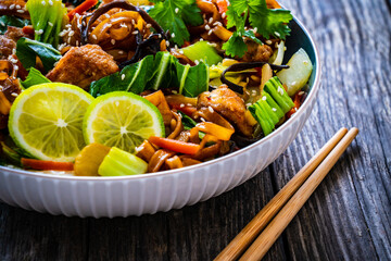 Asian food - chicken nuggets, noodles, stir fried vegetables, soy sauce and mushrooms on wooden table
