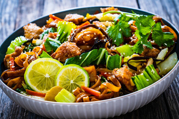 Asian food - chicken nuggets, noodles, stir fried vegetables, soy sauce and mushrooms on wooden...