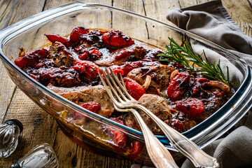 Roast pork loin with plums in sauce in glass cooking pan on wooden table
