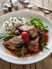 Roast pork loin with plums in sauce and white rice on wooden table
