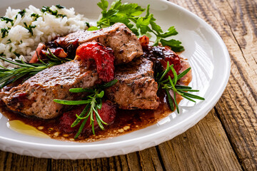 Roast pork loin with plums in sauce and white rice on wooden table
