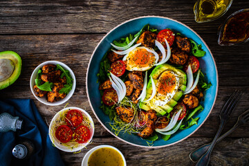 Tasty salad - fried chicken breast, avocado, boiled eggs, mini tomatoes and fresh green vegetables on wooden background
