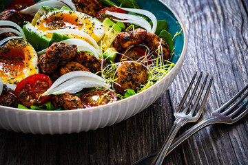 Tasty salad - fried chicken breast, avocado, boiled eggs, mini tomatoes and fresh green vegetables on wooden background
