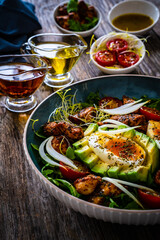 Tasty salad - fried chicken breast, avocado, boiled eggs, mini tomatoes and fresh green vegetables on wooden background
