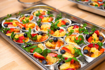 many portions Creme brulee decorated with fresh strawberries, blueberries and mint leaves