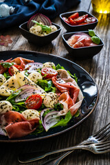 Fresh salad - prosciutto di Parma, mozzarella, pear and leafy vegetables on wooden table
