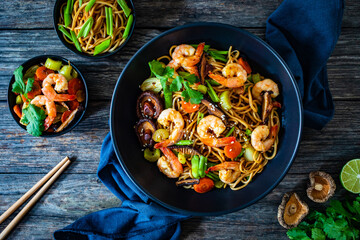 Mie noodles with fried prawns, shiitake mushrooms, coriander, carrot and celery on wooden table
