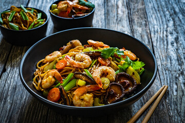 Mie noodles with fried prawns, shiitake mushrooms, coriander, carrot and celery on wooden table
