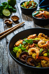 Mie noodles with fried prawns, shiitake mushrooms, coriander, carrot and celery on wooden table
