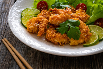 Fried panko prawns with lime, tomatoes and greens wooden table
