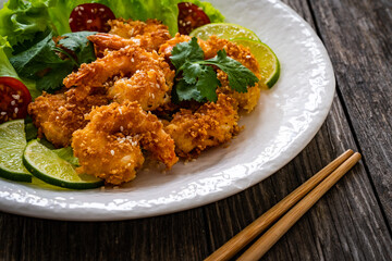 Fried panko prawns with lime, tomatoes and greens wooden table
