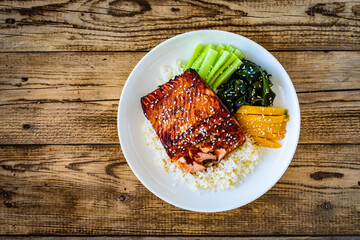 Fried teriyaki salmon steak with white rice, mango, cucumber and wakame on wooden table
