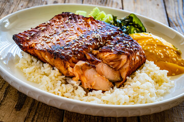Fried teriyaki salmon steak with white rice, mango, cucumber and wakame on wooden table
