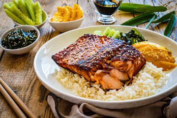 Fried teriyaki salmon steak with white rice, mango, cucumber and wakame on wooden table
