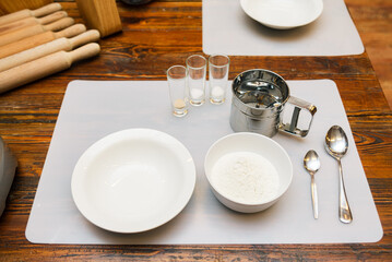 a table with a set of kitchen utensils for preparing dough. flour, yeast, bowls, spoons, rolling pins