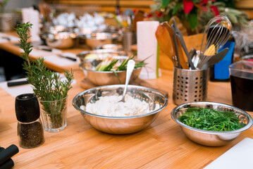 Kitchen table with raw ingredients and cooking tools like spatulas, tongs, and whisk.