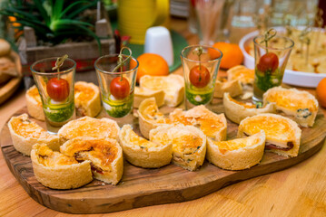 Catering appetizers on the table. Shot glasses with caprese canapés and slices of mini Quiché with sun-dried tomatoes