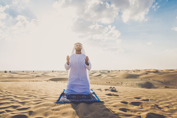 Arab man wearing typical middle eastern clothing in the desert praying for ramadan celebration