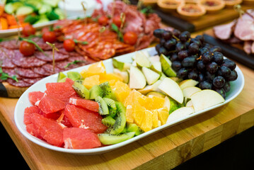 A plate of sliced fruit on the snack table. slices of kiwi, grapefruit, pear and grapes.