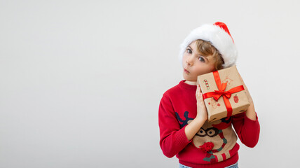 Excited funny German caucasian child girl boy wear red Santa hat holding Christmas gift boxes dreaming over white background. Copy space. Merry Christmas presents shopping sale.