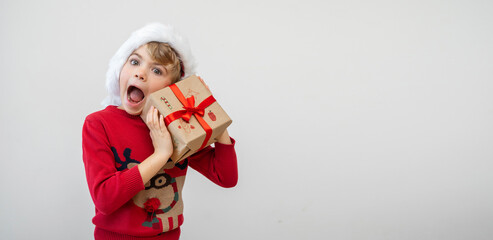 Obraz premium Excited funny Canadian caucasian child girl boy wear red Santa hat holding Christmas gift boxes dreaming over white background. Copy space. Merry Christmas presents shopping sale.