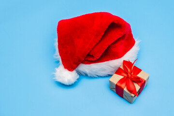 A red Santa Claus hat and gift boxes tied with ribbons on a blue background. Christmas card. Copy space. Space for text. Minimalism