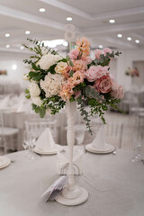 Centerpiece made of green leaves and fresh flowers stands on the dinner table. Wedding day. Fresh flowers decorations. Peony arrangements.