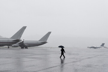 A man under an umbrella at the airport. Desert airfield. Rainy weather at the airport. Large airfield with aircraft. The man goes to the plane.