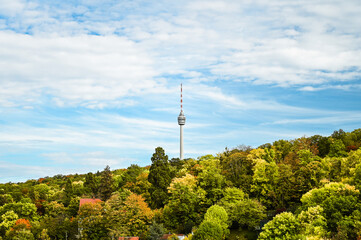 Autumnal view of the Stuttgart TV tower under a partly cloudy sky. The TV tower is surrounded by colorful forest.