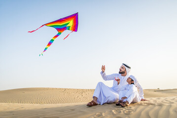 Playful arab man and his son wering traditional middle eastern emirate clothing playing and having...