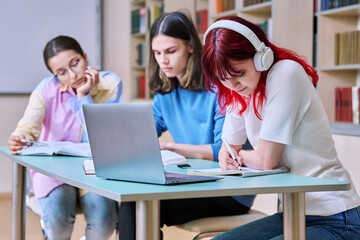 Group of teenage students study at their desks in library class