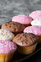 Cupcakes, decorated with icing and sprinkles on a black serving dish. On a dark concrete background