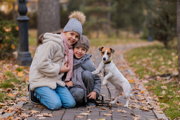 Caucasian boy and girl posing sitting on sidewalk with jack russell terrier dog in park in autumn.