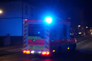 Rettungsdienstwagen mit blauem und goldgelben Lichtern fährt auf Straße vor weißem Haus in Stadt...