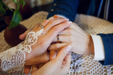 Newlyweds bride and groom with a beautiful manicure gently hold hands as a new family with wedding gold rings at a table in a cozy cafe expressing their love