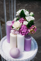 Wedding bouquet for the bride of white and yellow roses and other flowers, multi-colored candles on a wooden decorative white table, outdoors.
