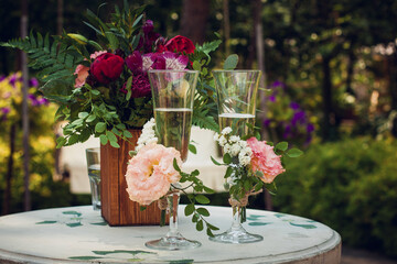 Glasses with champagne wine drink on a white wooden table decorated with white, pink and red flowers in a wooden brown vase, at a wedding banquet, for newlyweds, in a summer garden.