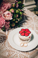 Stylishly decorated cake with a red flower pattern in a white plate with wedding rings on the table with a bouquet for the bride on the wedding day in the morning at breakfast